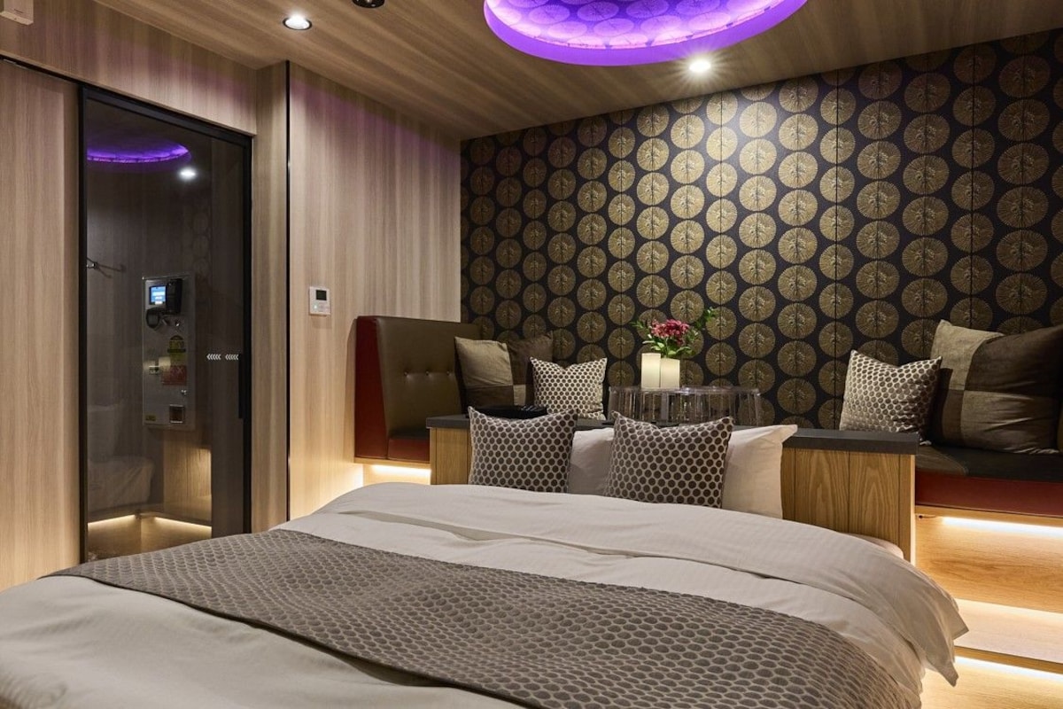 A modern bedroom with a large bed, a bedside table with a lamp, and a wall with a patterned wallpaper.