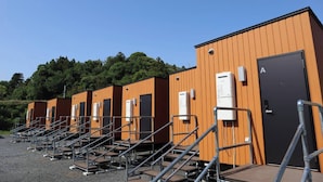 Filera de cabines portàtils de fusta, amb quadres elèctrics exteriors, baranes de metall i una porta marcada amb la lletra 'A'.