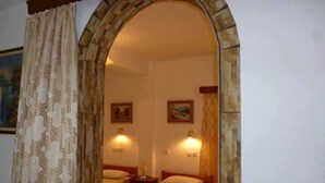 A room with a stone archway, two beds, wall-mounted lamps, and a painting. - Vasilis Ios Place Room 1 (Chora)