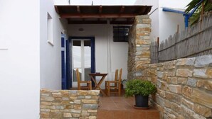 A narrow staircase leading to a door with a blue shutter, a small outdoor table with chairs, and a potted plant. - Vasilis Ios Place Room 1 (Chora)