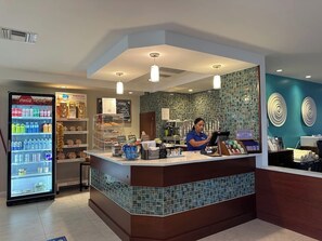 Eine Hotelhalle mit einer Rezeption, einem Coca-Cola-Kühlschrank und einer gefliesten Wand mit kreisförmigen Mustern.