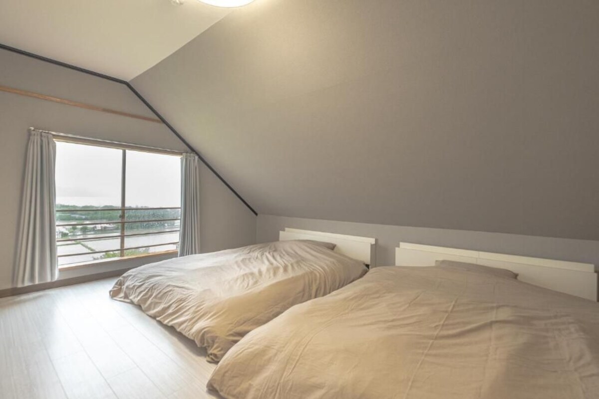 A bedroom with two beds, a sloped ceiling, and a large window with curtains.