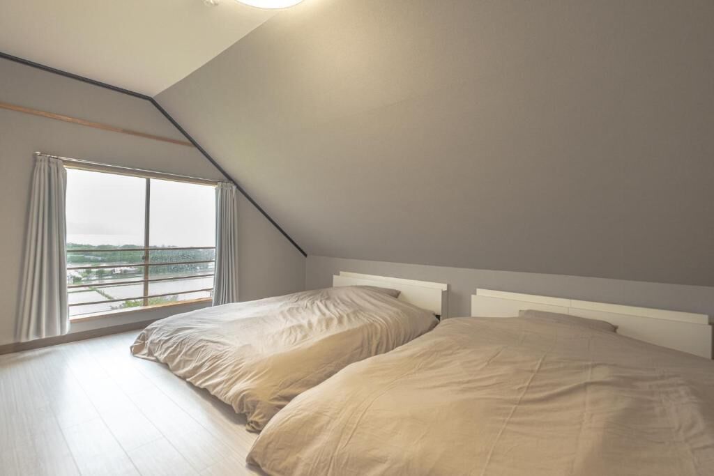 A bedroom with two beds, a sloped ceiling, and a large window with curtains.