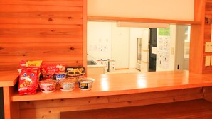 A wooden reception desk with snacks and a view into a room with a refrigerator and a bulletin board. - Aya no Yado Fusen (Shirahama)