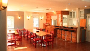 A spacious dining area with a long wooden table and red chairs, a bar with stools, and a kitchen area with wooden cabinets. - Aya no Yado Fusen (Shirahama)