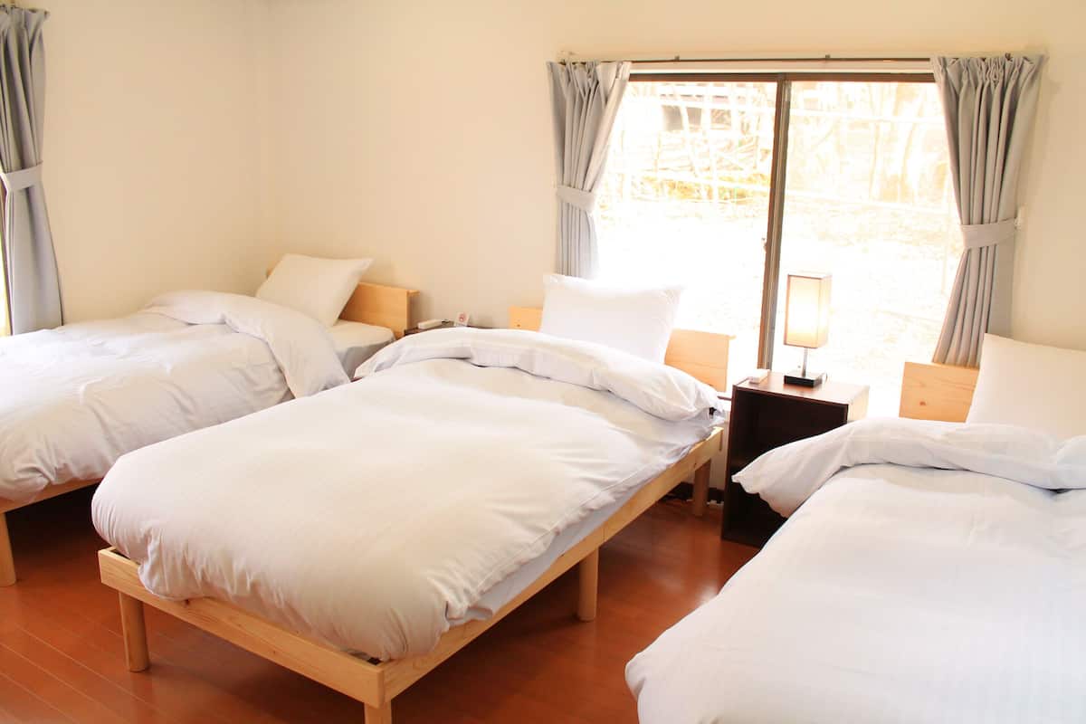 Quarto de hotel com duas camas de solteiro, uma mesa de cabeceira com abajur e uma janela com cortinas.