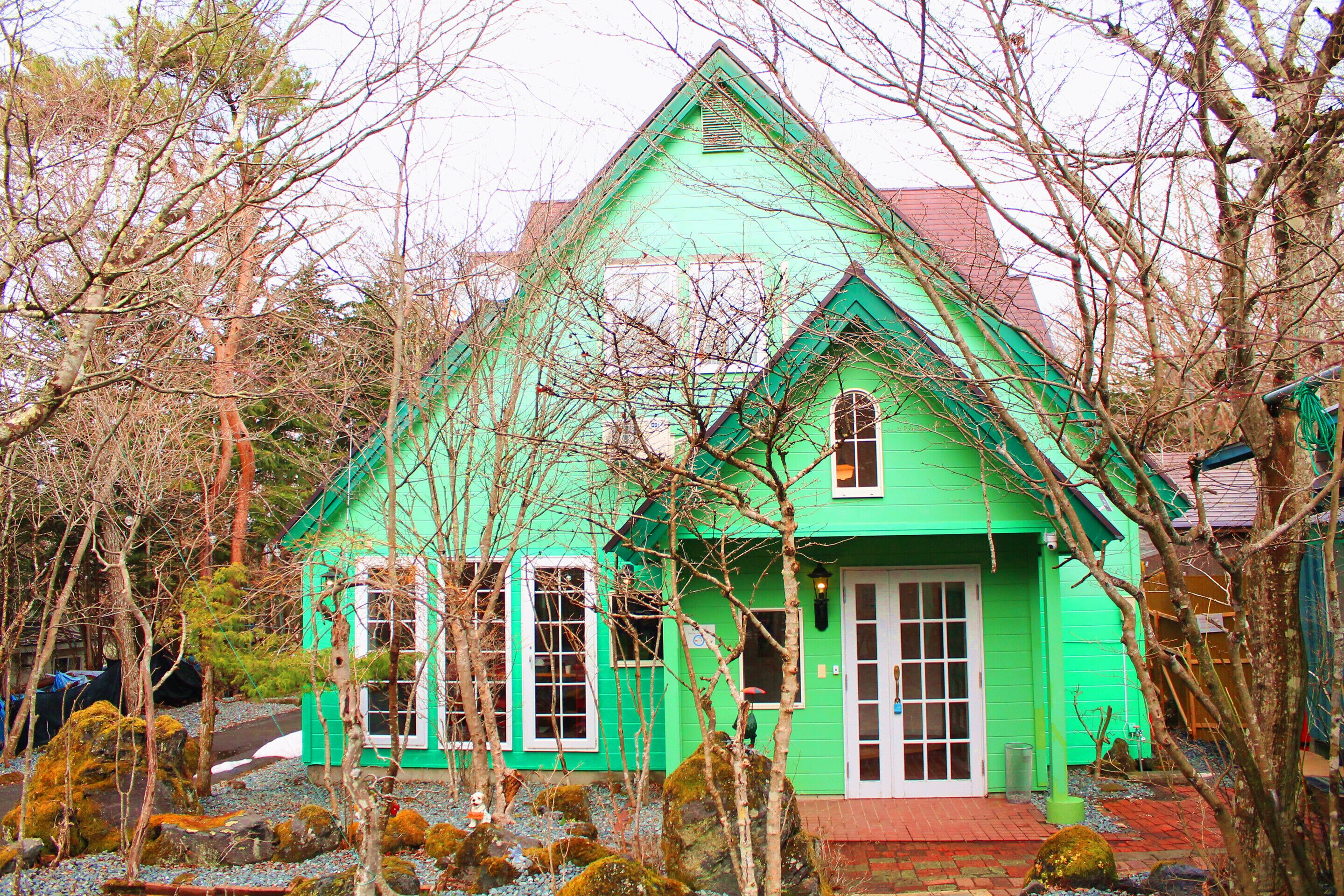 Ein grünes Haus mit rotem Dach, umgeben von Bäumen und Felsen.