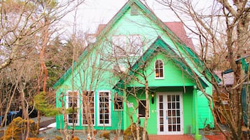 A green house with a red roof, surrounded by trees and rocks.