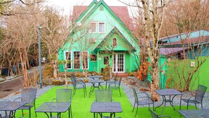 A green house with a red roof, surrounded by a garden with artificial grass and metal tables and chairs. - Aya no Yado Fusen (Shirahama)