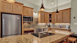 A kitchen with wooden cabinets, a stainless steel refrigerator, a microwave, an induction cooktop, and a granite countertop. - Crazy Horse-Close to Canyon Lake Marina! (Canyon Lake)