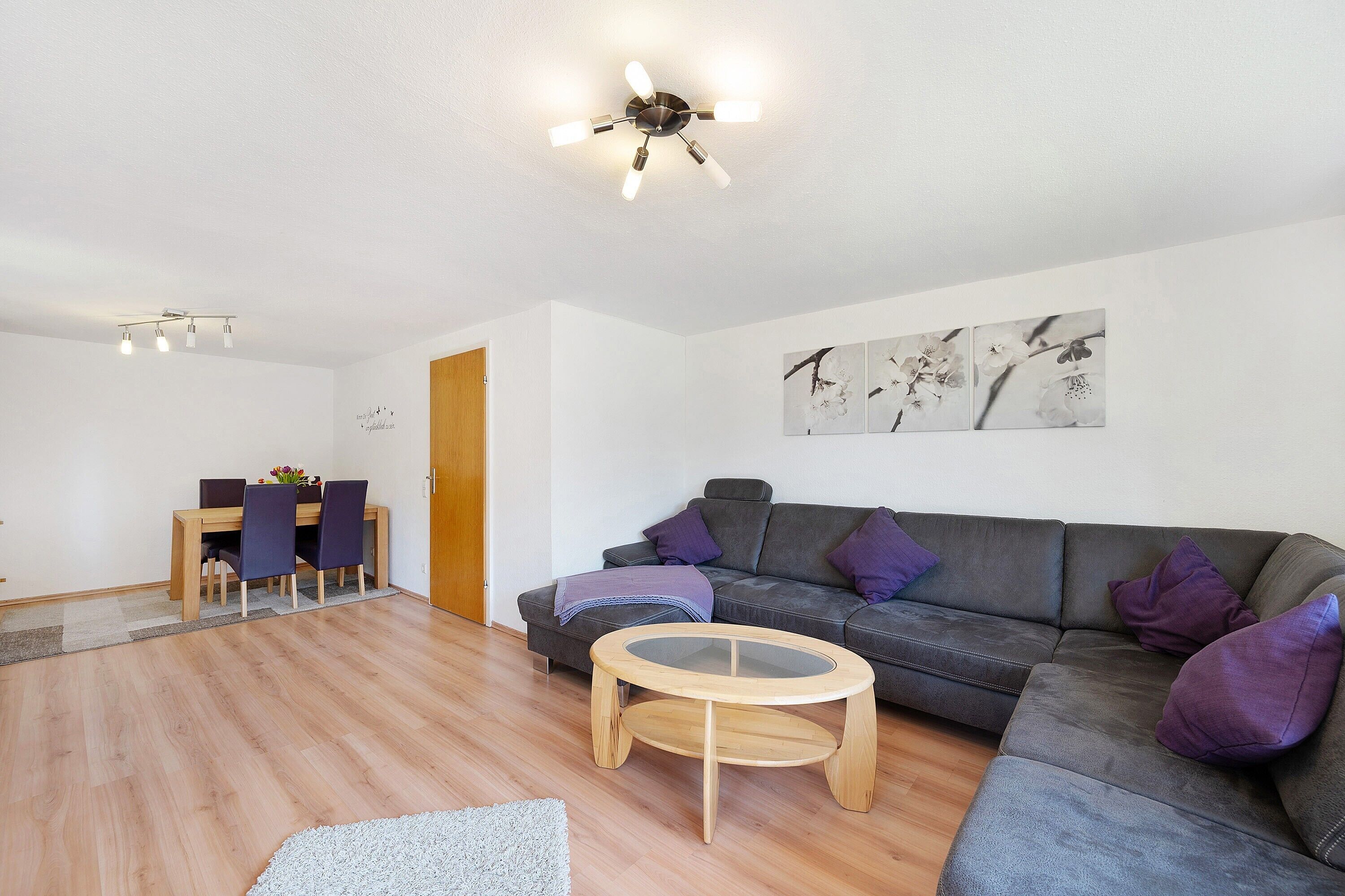 A modern living room with a wooden dining table, a grey sofa, and a round coffee table.