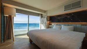 Een hotelkamer met een groot bed, uitzicht op de oceaan, een marmeren hoofdeinde en een groot raam.