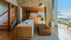 Een modern interieur met een stenen muur, een houten trap, een bank, een salontafel en uitzicht op de stad.