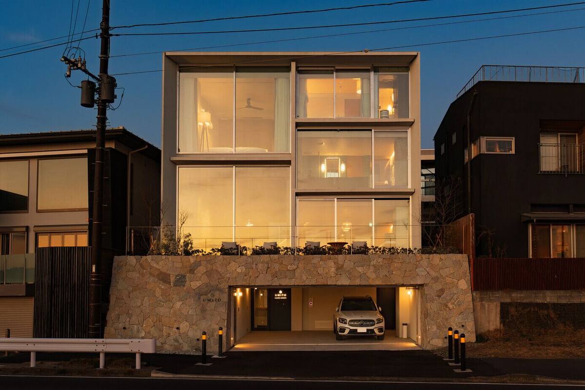 Un edificio moderno de dos plantas con fachada de piedra, ventanas grandes y un automóvil estacionado en un garaje subterráneo.