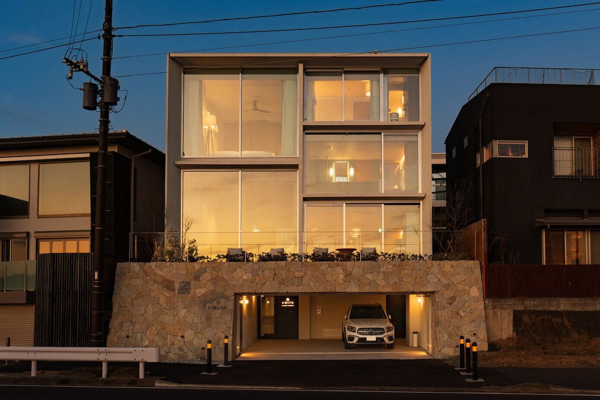 Un edificio moderno de dos plantas con fachada de piedra, ventanas grandes y un automóvil estacionado en un garaje subterráneo.