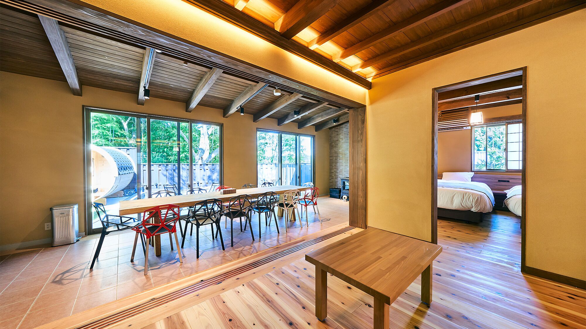 Una habitación amplia con una larga mesa de madera, varias sillas y una cama en la habitación contigua.