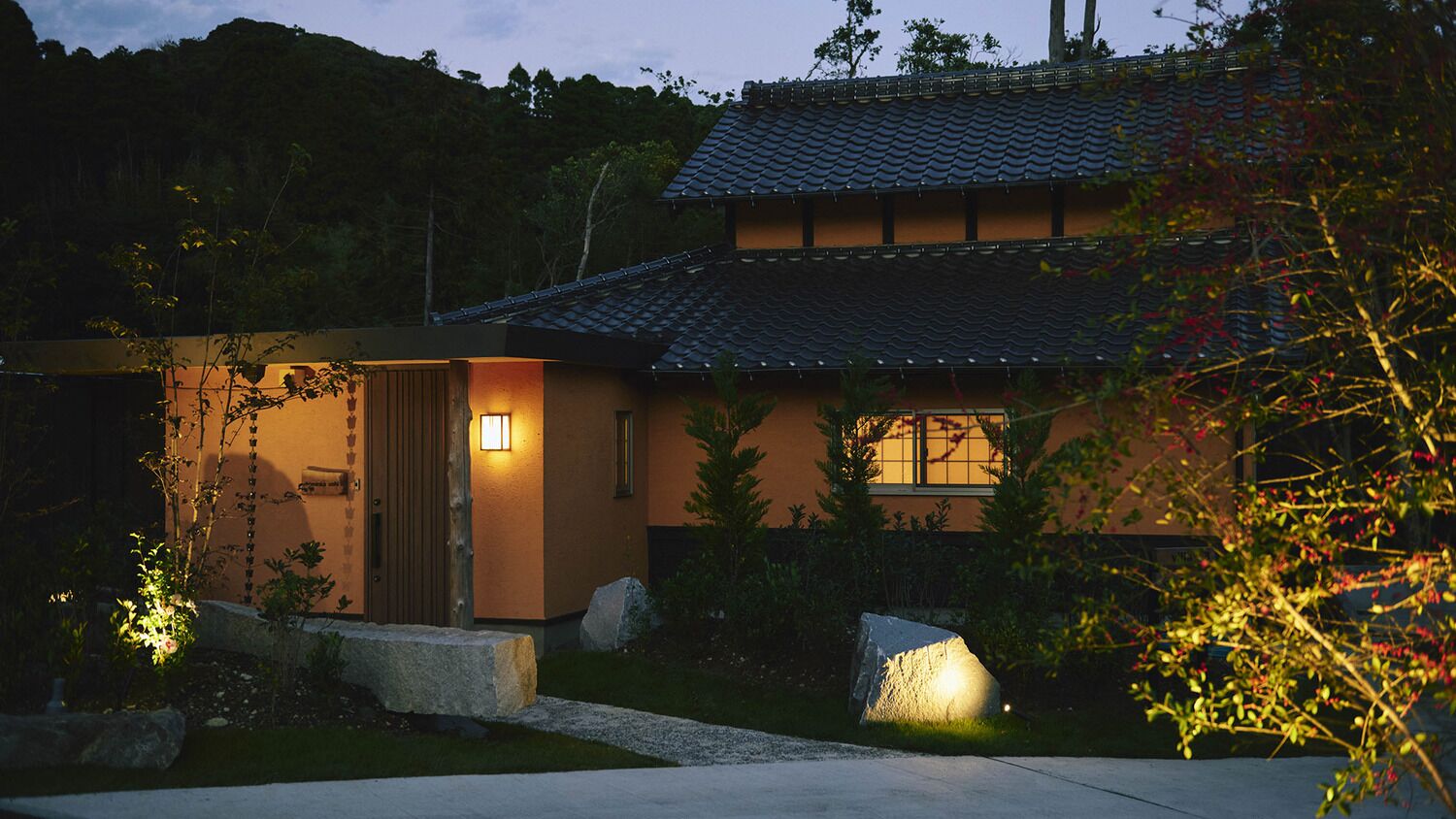 Una casa tradicional japonesa con techo de tejas, puerta de madera y un camino de piedra que lleva a la entrada.