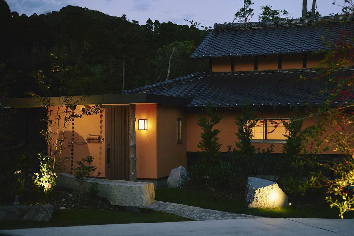 Una casa tradicional japonesa con techo de tejas, puerta de madera y un camino de piedra que lleva a la entrada.