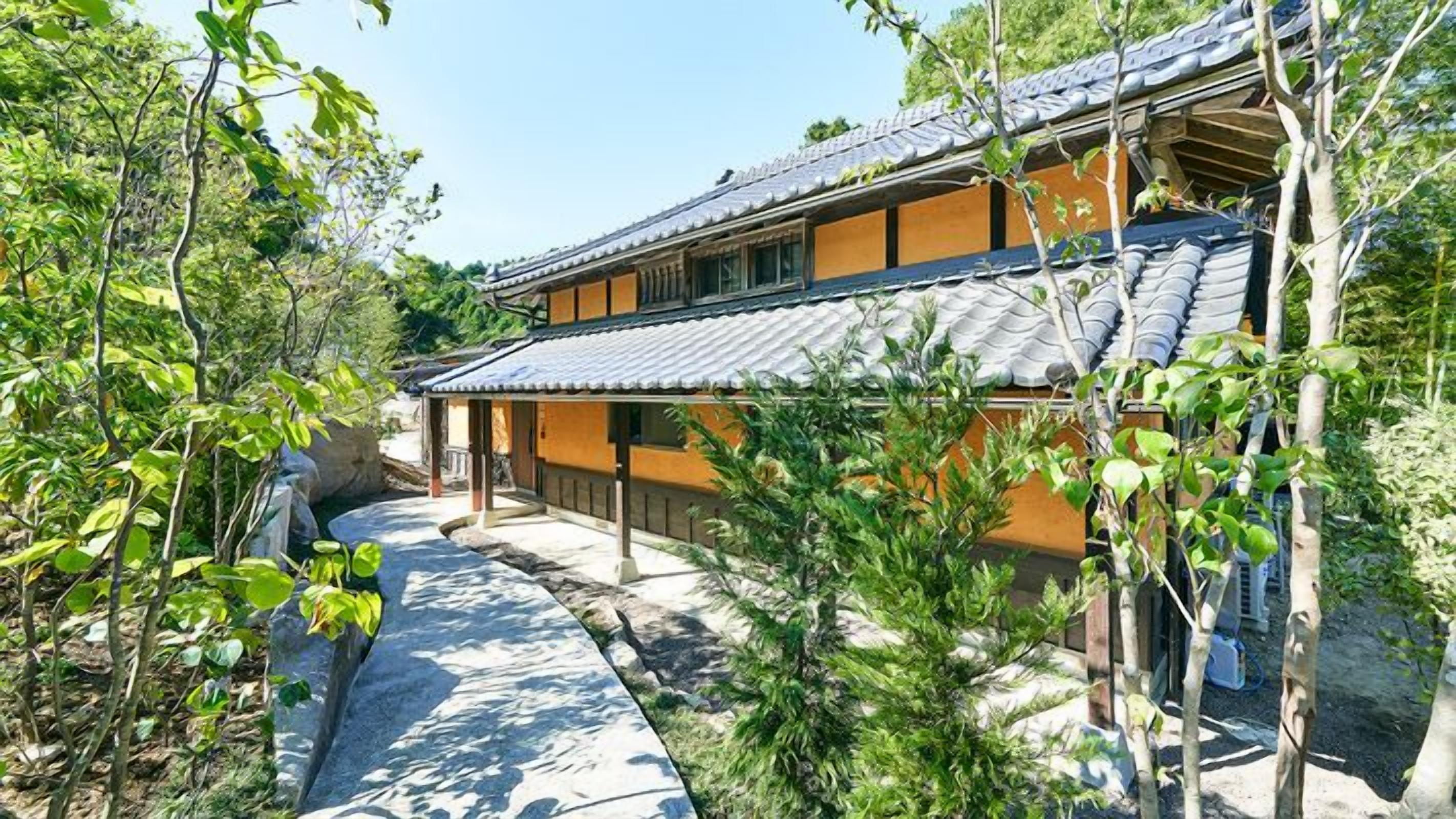 Un edificio japonés tradicional con tejado de tejas, rodeado de vegetación y un sendero de piedra.