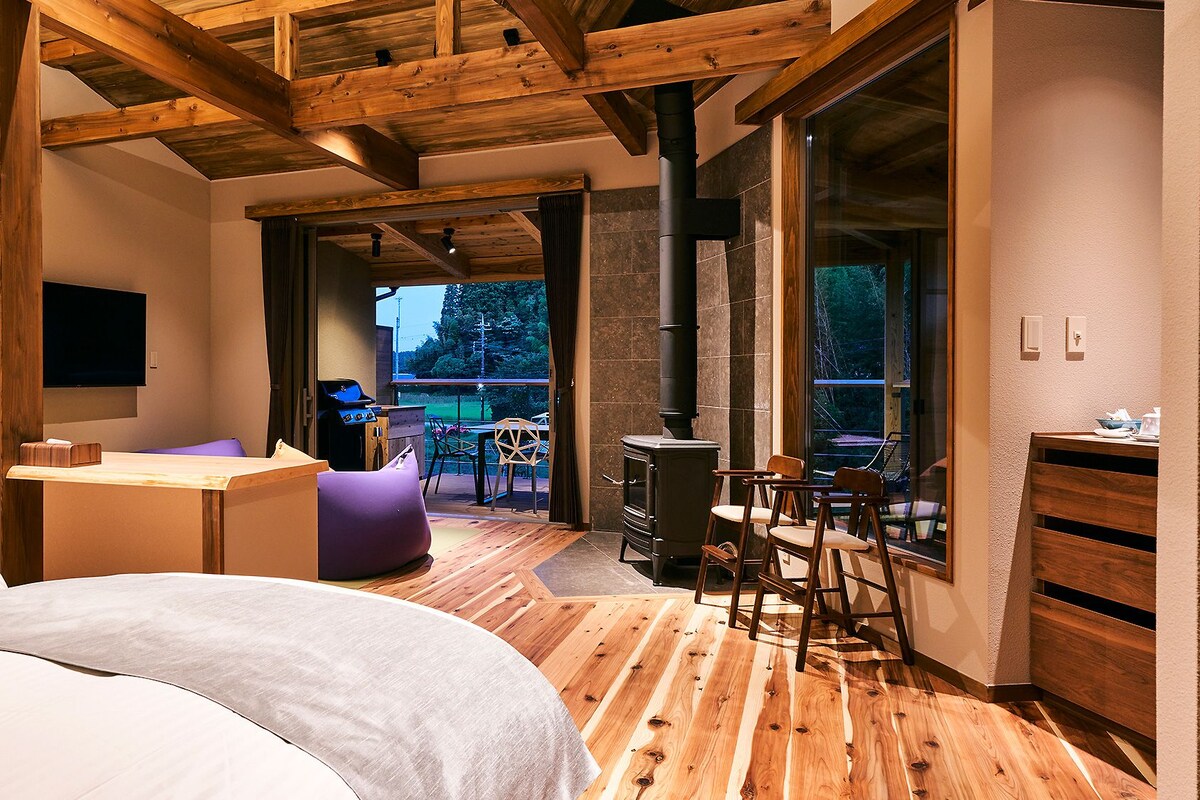 Un dormitorio moderno con techo de madera, una cama, un escritorio y vistas al exterior.