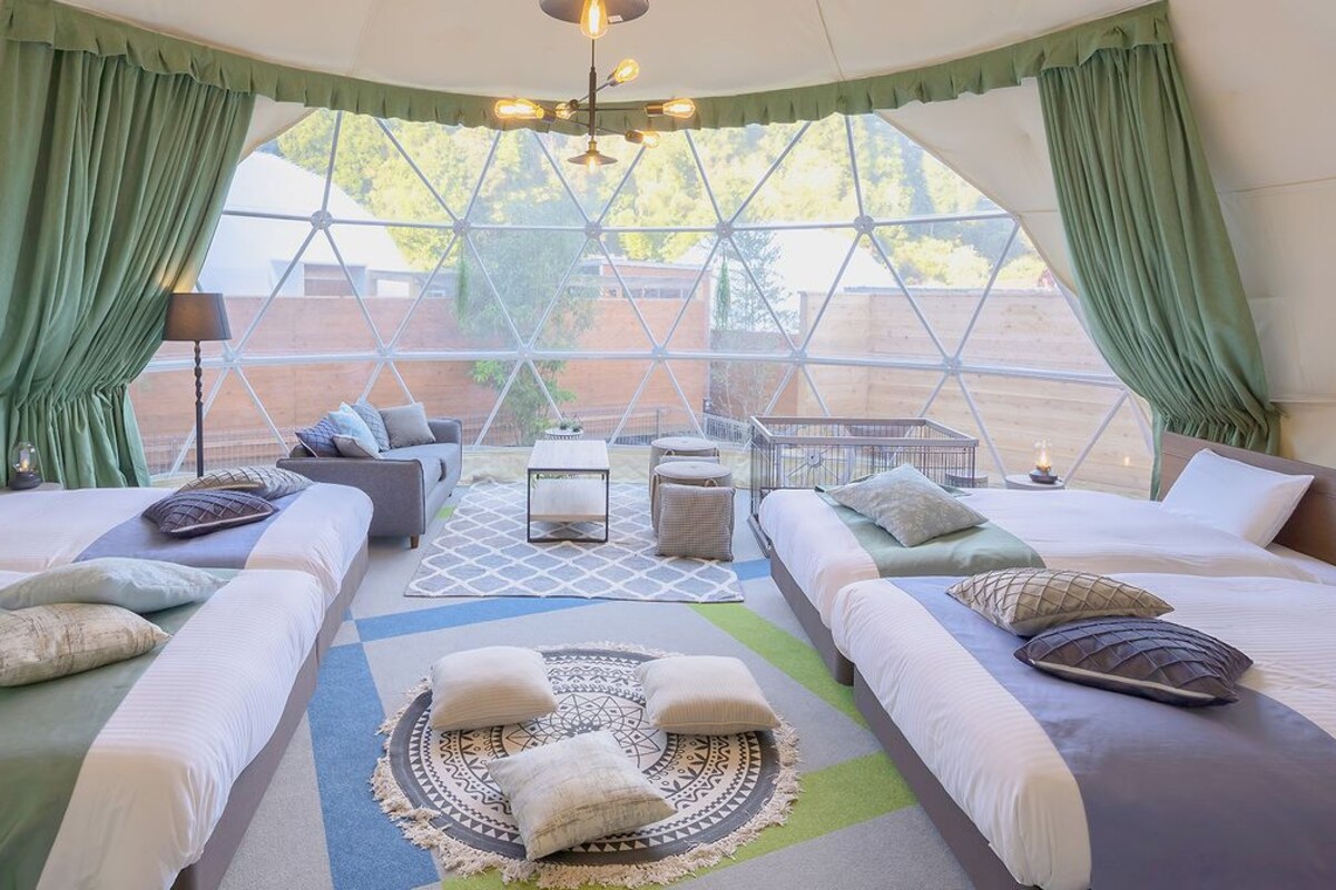 A cozy room with two beds, a sofa, a small table, and a view through large windows.