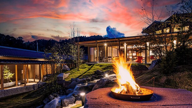 A modern house with a fire pit in the foreground, a waterfall, and a glass-enclosed dining area. - Itsukiri (Isumi)