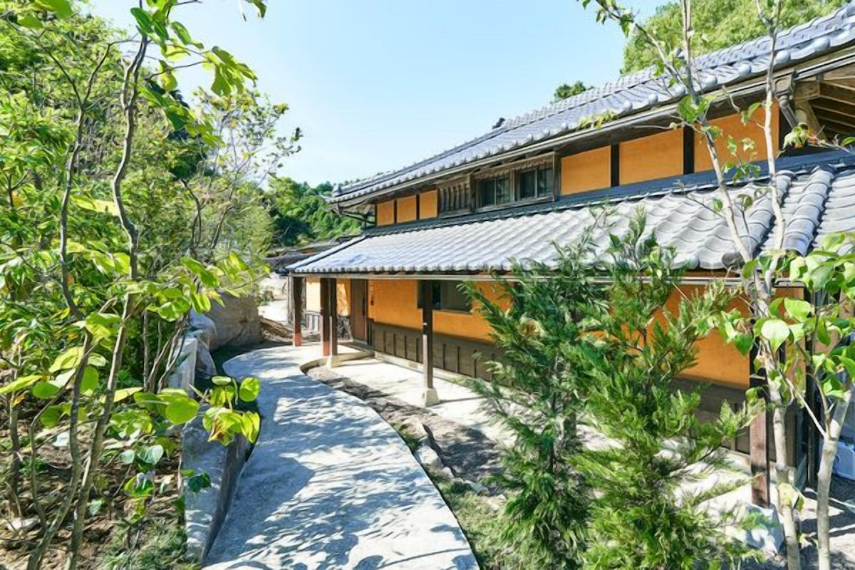 A traditional Japanese building with a tiled roof, surrounded by greenery and a stone pathway.