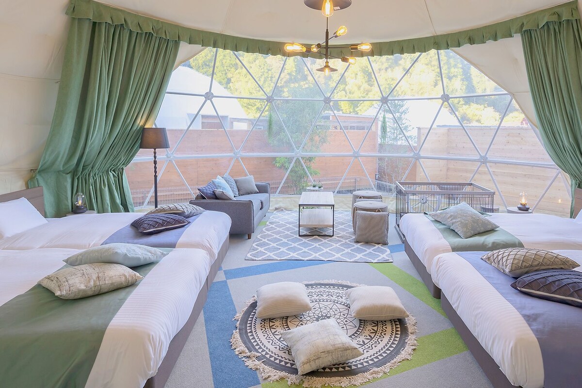 A room with two beds, a sofa, a coffee table, and a view through large windows.
