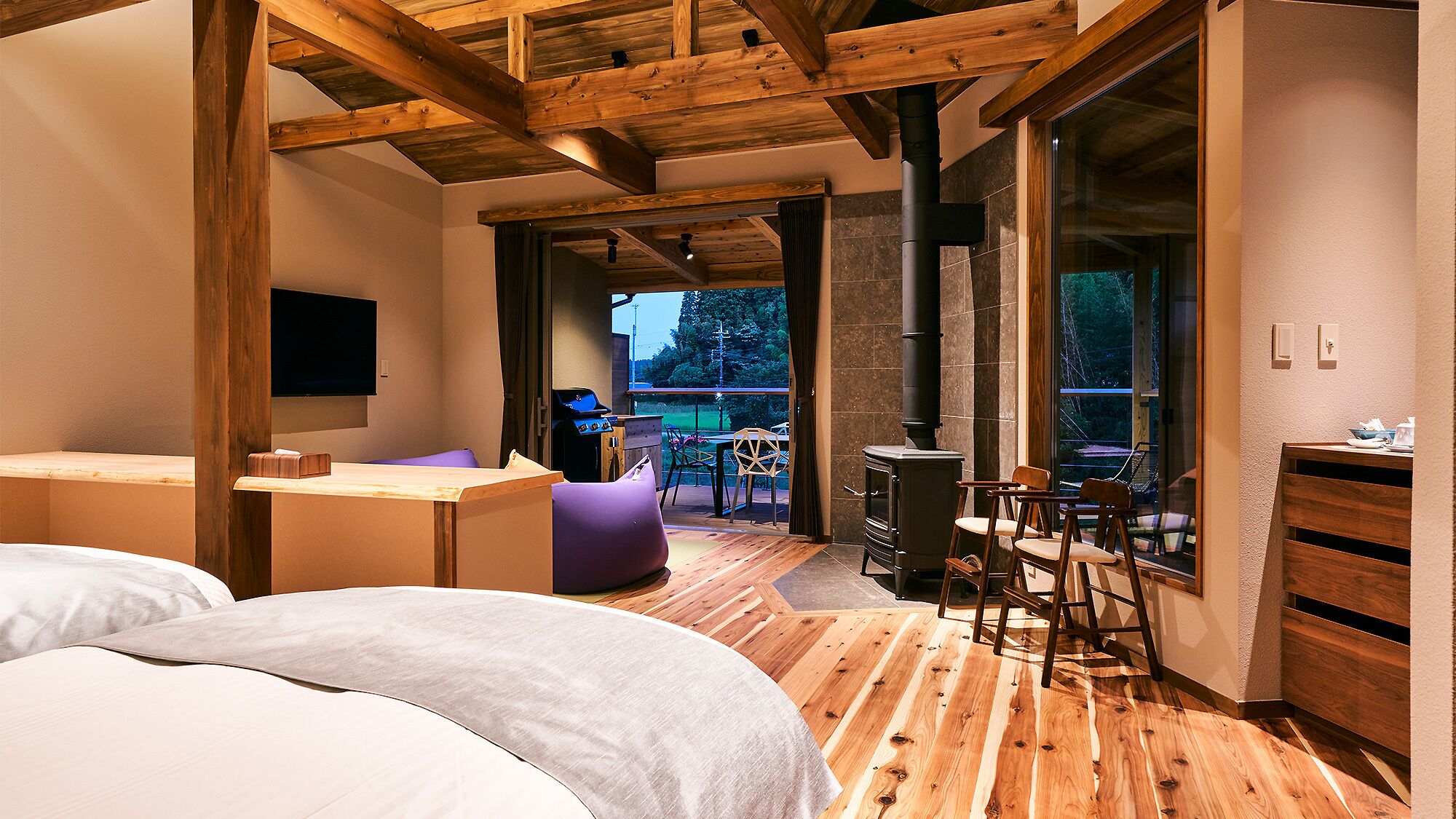 Un dormitorio moderno con techo de madera, una cama, un escritorio y vistas al exterior.
