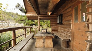 Une cabane en bois avec un porche couvert, une table, des bancs et un panneau indiquant qu’il est interdit de fumer.