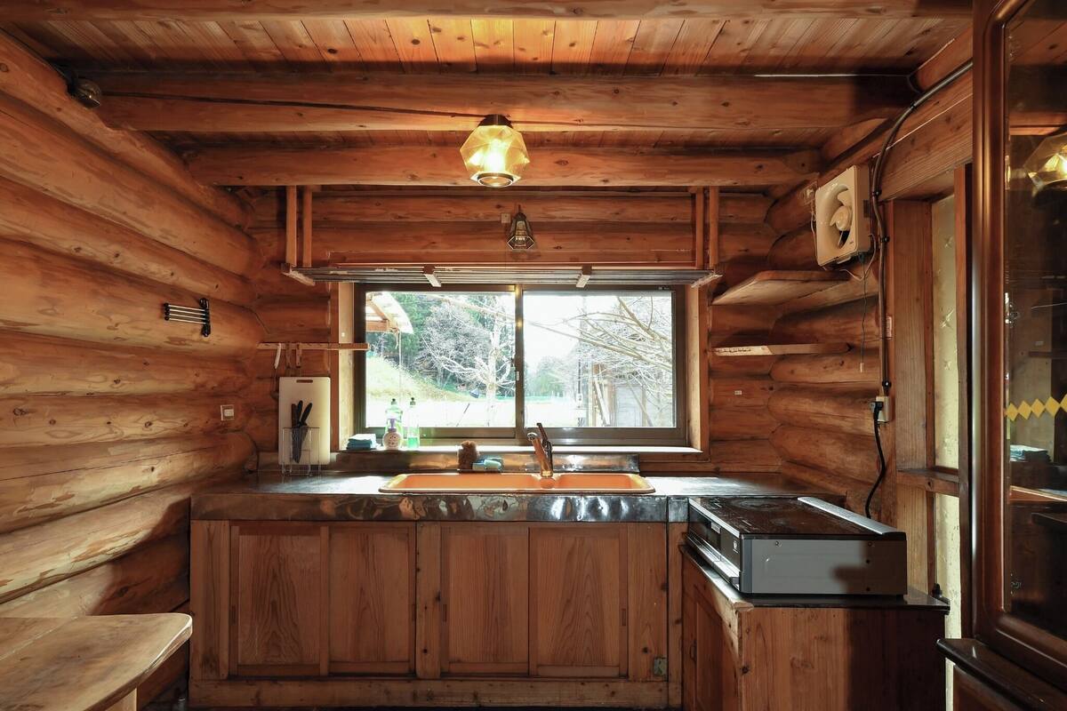 A wooden cabin interior with a kitchen area, including a sink, cabinets, and a stove.