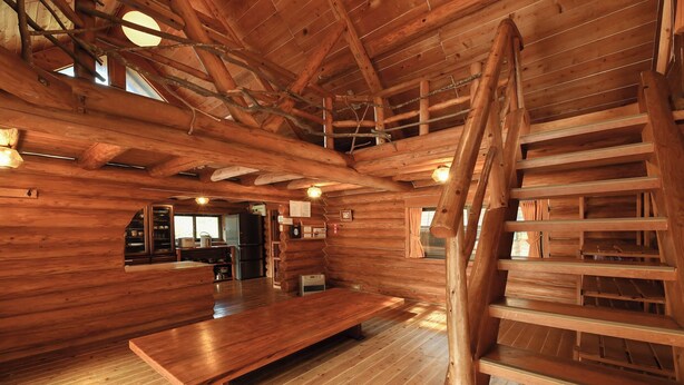 L’intérieur d’une cabane en rondins, avec une table à manger en bois, un escalier et un coin cuisine.