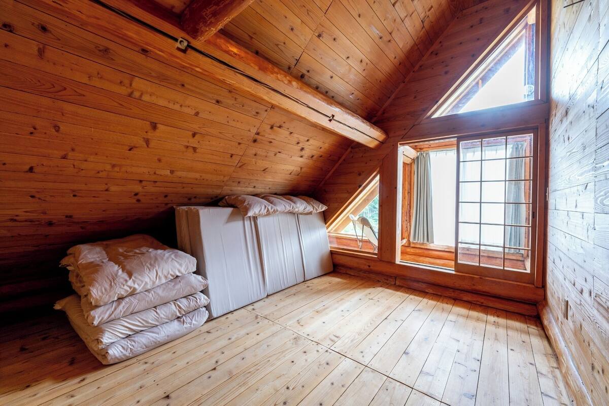 A wooden cabin with a loft bed, a window with curtains, and a wooden floor.