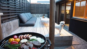 Eine Terrasse mit Grill, einem Hund und einer Sitzgelegenheit.