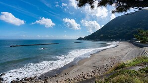 Una spiaggia con un litorale roccioso, cielo sereno e una montagna sullo sfondo.