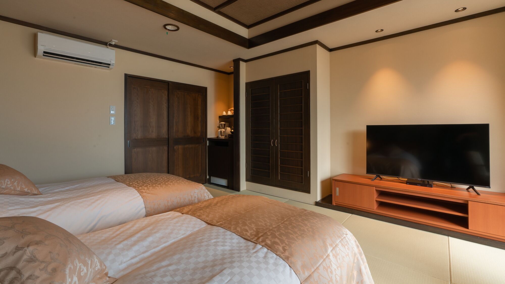 A hotel room with two beds, a TV, a wardrobe, and a sliding door.