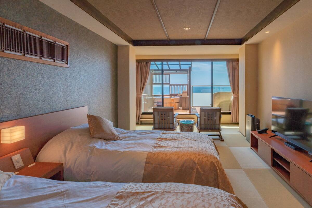 Quarto de hotel com duas camas, televisão,  área de estar com vista para o mar e varanda.