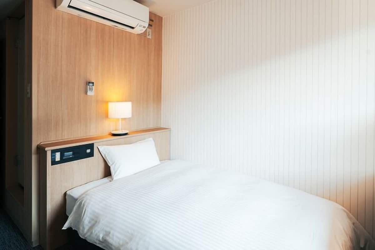 Ein Hotelzimmer mit Bett, Nachttischlampe, Klimaanlage und Fernseher.