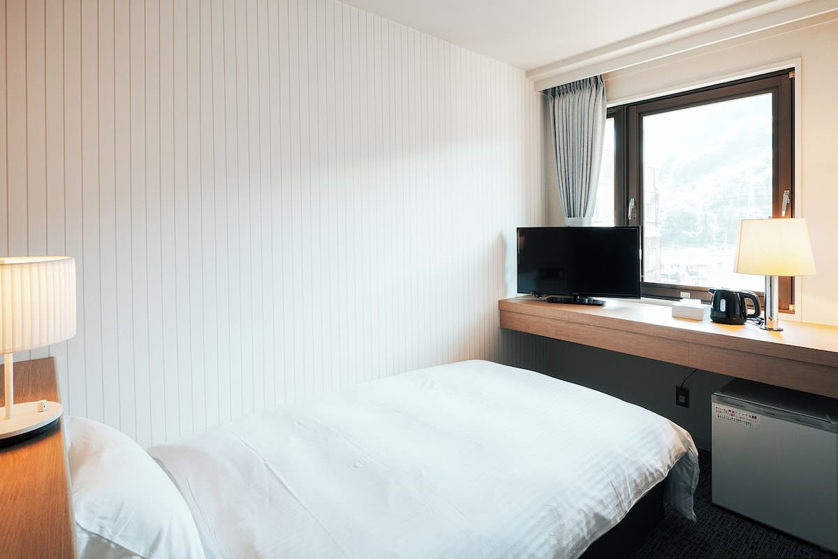 Ein Hotelzimmer mit Bett, Schreibtisch mit Fernseher, Lampe und Fenster mit Vorhängen.