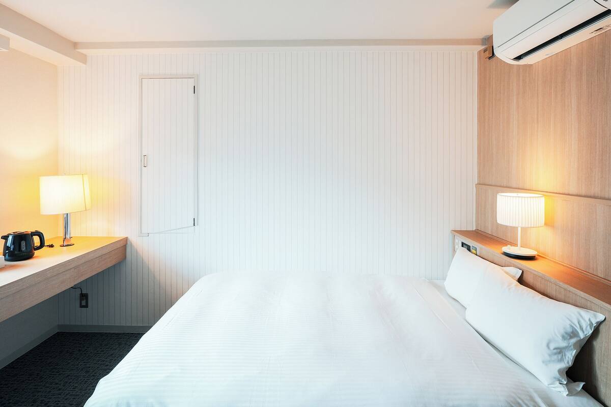 Ein Hotelzimmer mit einem Bett, zwei Nachttischen mit Lampen, einer Kaffeemaschine, einer Taschentuchbox und einer Klimaanlage.