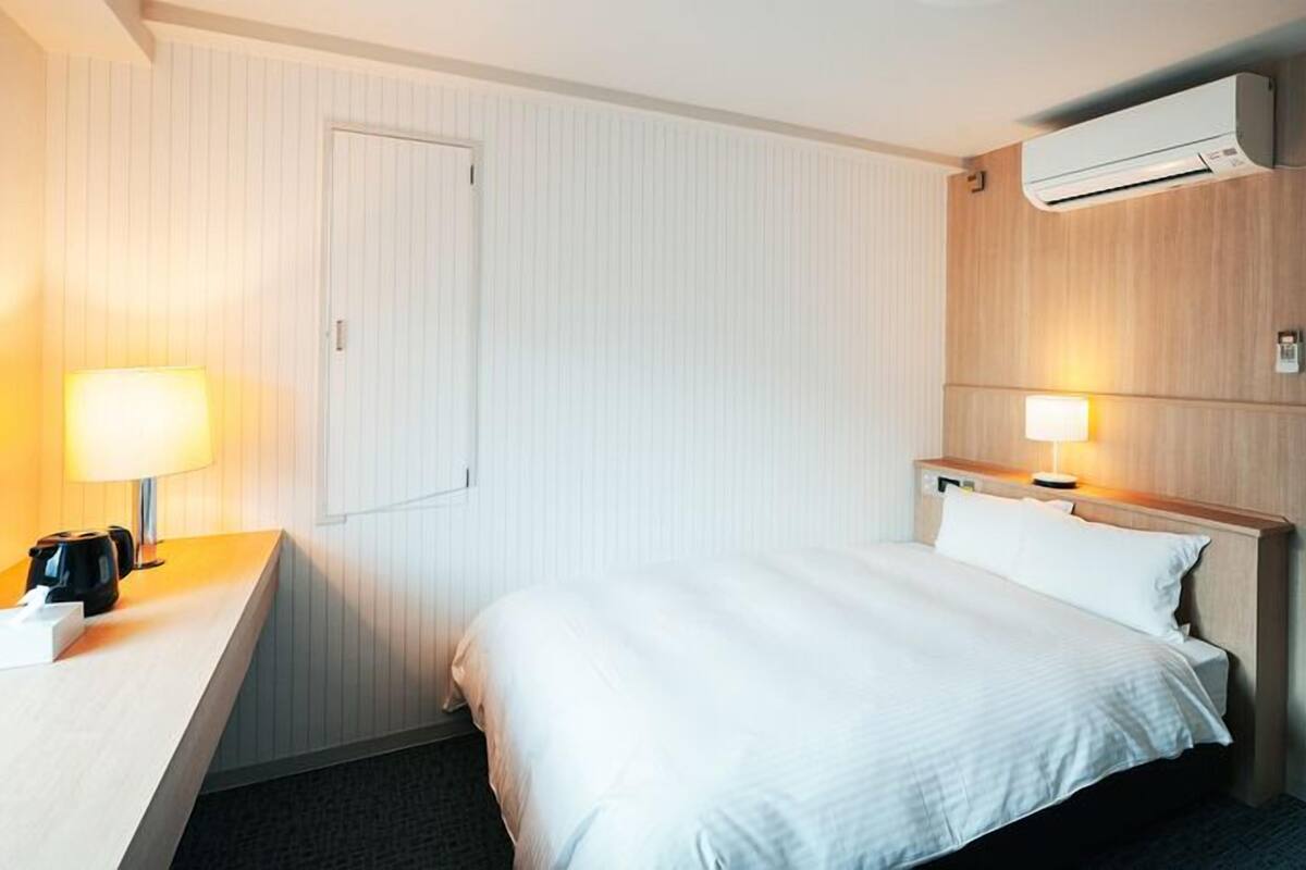 Ein Hotelzimmer mit Bett, Nachttisch, Lampe, Klimaanlage und einer Tür.