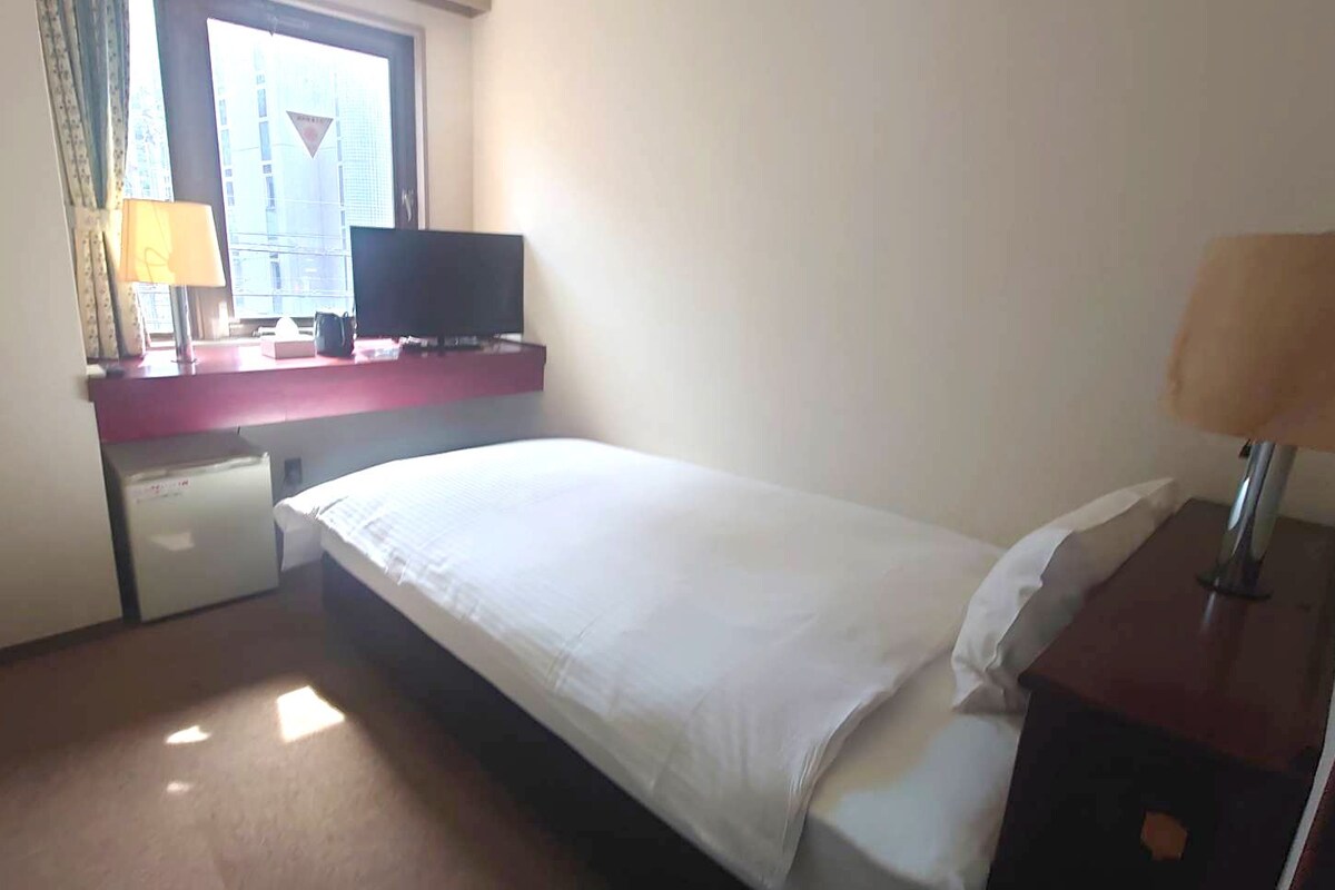 A hotel room with a bed, a desk with a computer, a TV, and a window.