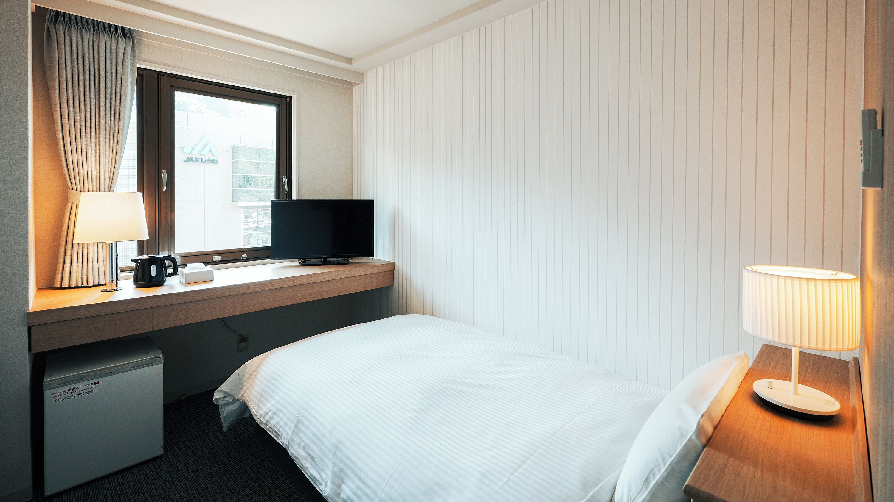 A hotel room with a bed, a desk with a television, a lamp, and a coffee maker.