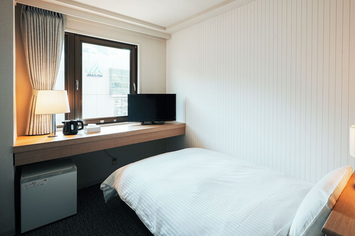 Ein Hotelzimmer mit einem Bett, einem Schreibtisch mit Fernseher, einer Lampe und einer Kaffeemaschine.