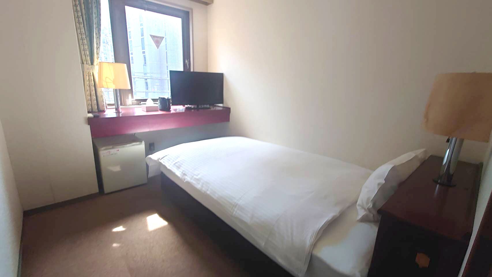 A hotel room with a bed, a desk with a computer, a television, and a window with curtains.