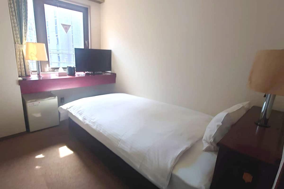 Ein Hotelzimmer mit Bett, Schreibtisch mit Computer, Fernseher und einem Fenster mit Vorhängen.