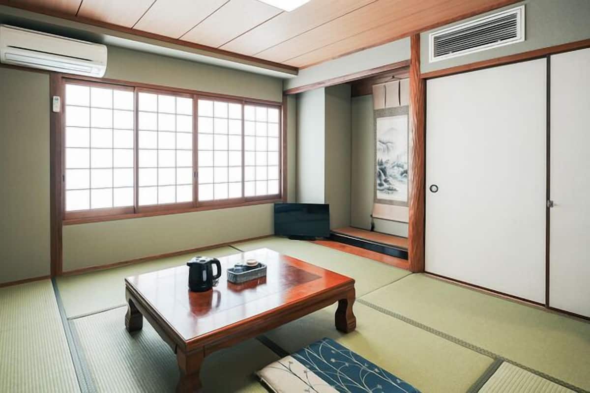 Ein traditioneller japanischer Raum mit Tatami-Böden, einem niedrigen Holztisch, einem Fernseher und gleitenden Türen.