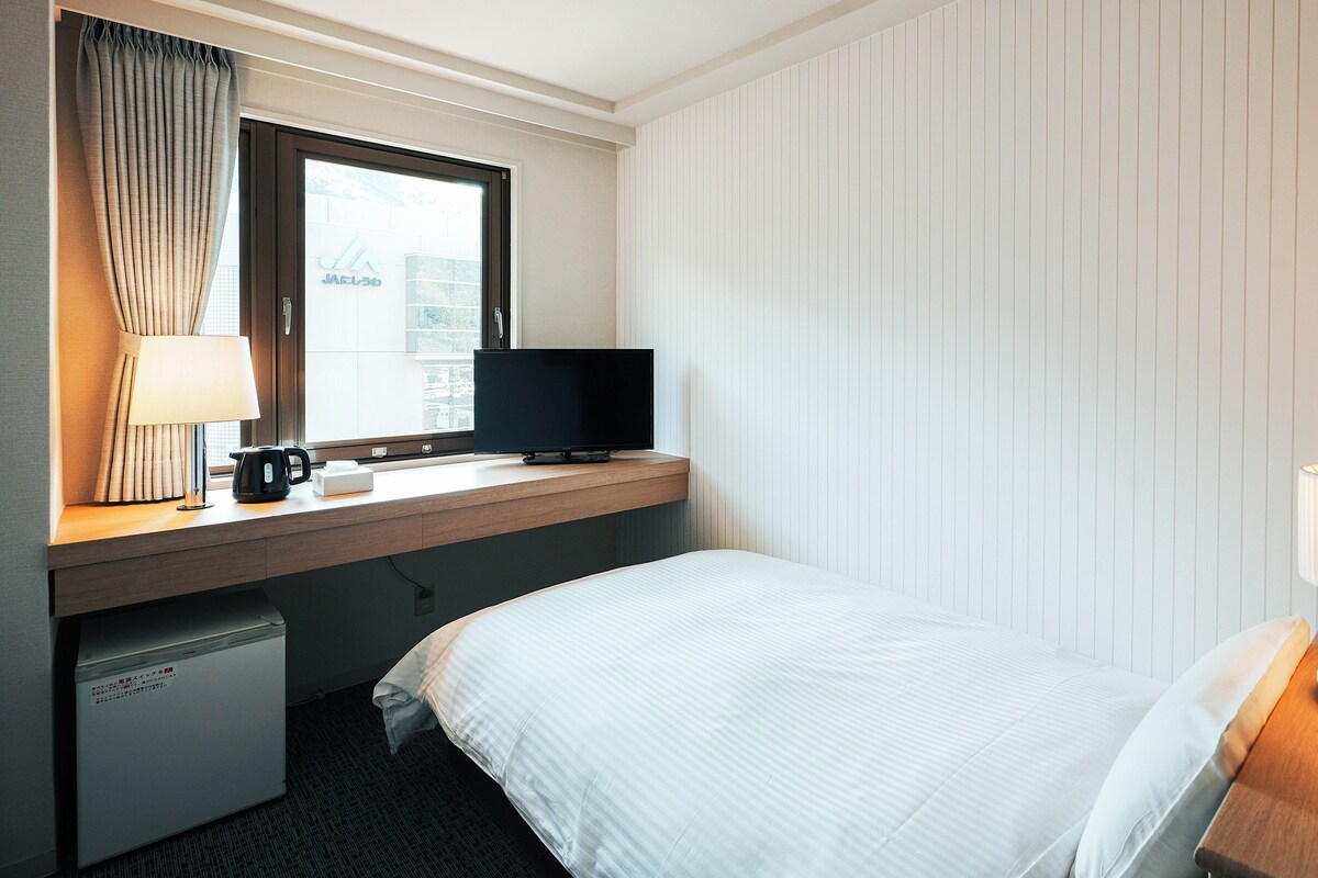 A hotel room with a bed, a desk with a television, a lamp, and a coffee maker.