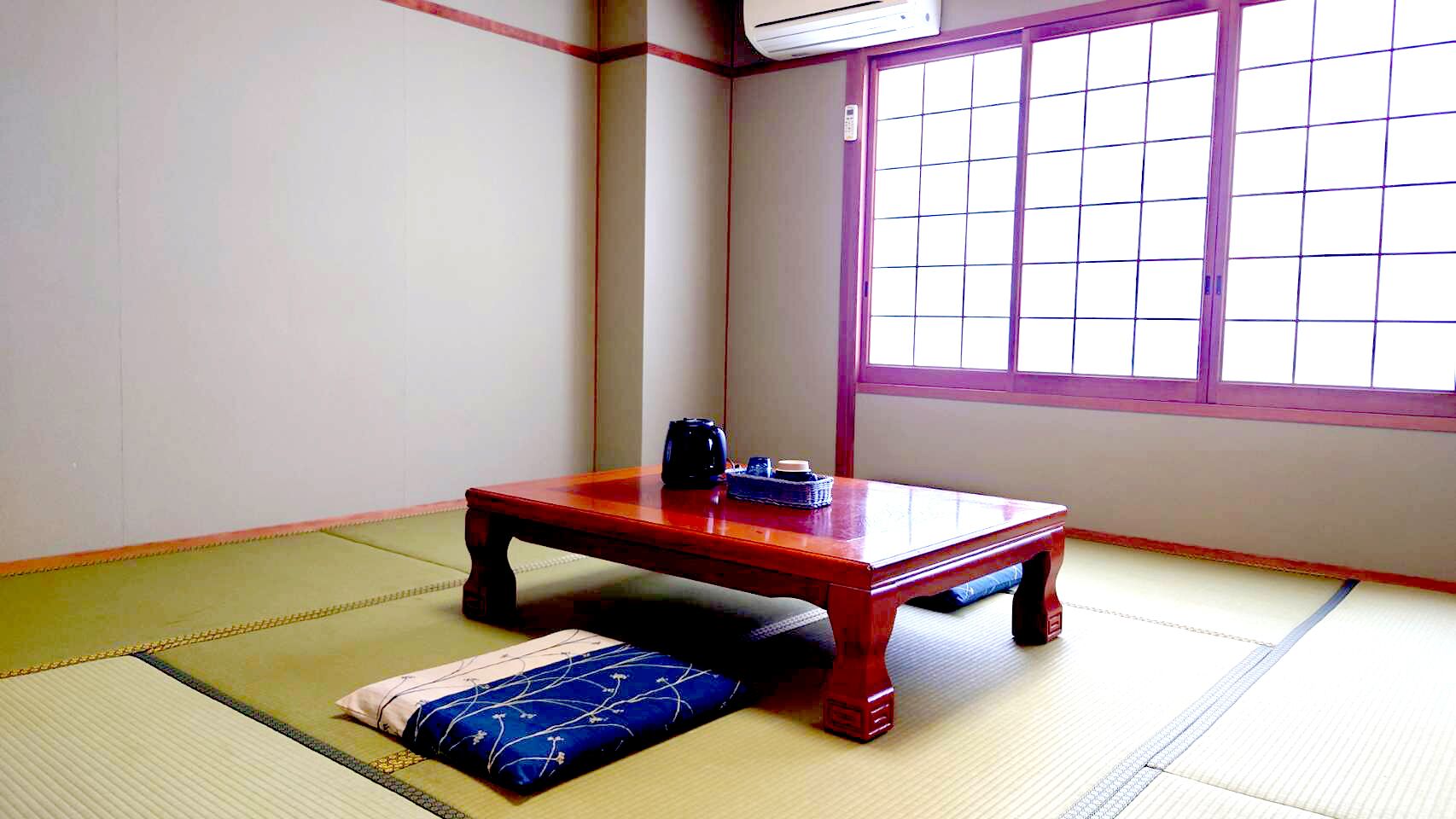 A tatami mat room with a low wooden table, a cushion, and a window with grid panes.