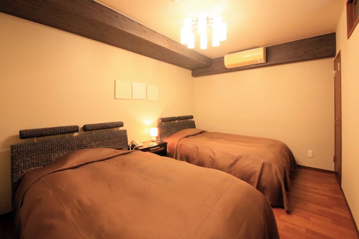 Une chambre avec deux lits, une table de chevet avec une lampe, un climatiseur et une poutre en bois au plafond.